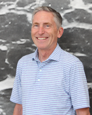 Jerry smiling for a headshot in front of a gray background