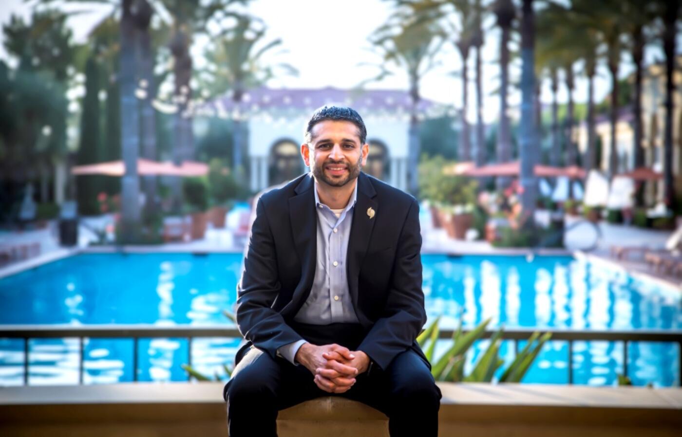 Ravi posing in a suit with a pool behind him.