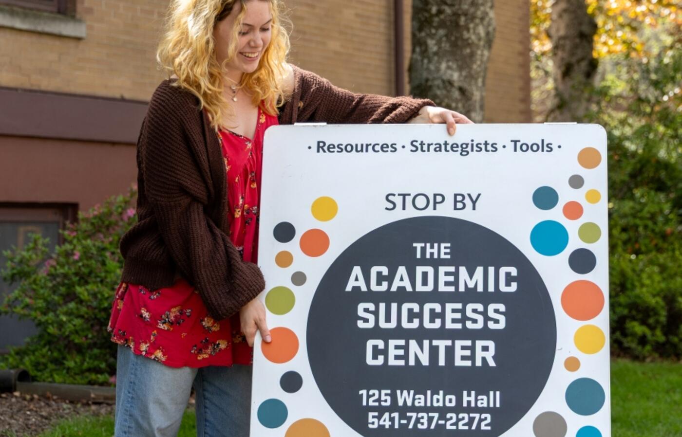 Student placing an Academic Success Center sign on the ground.