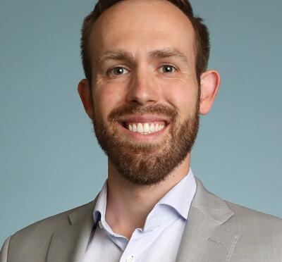 Headshot of Dylan in a light grey suit