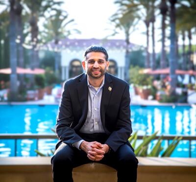 Ravi posing in a suit with a pool behind him.