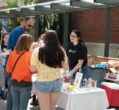 Honors student engages community members at the Honors College table during the Dam Proud Day Street Fair, where honors students sold dirty sodas to raise funds for HC student scholarships.