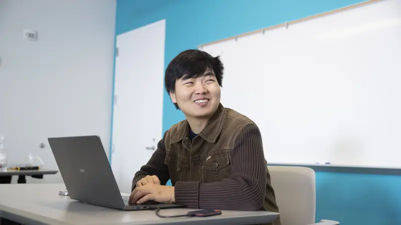 Male HC student smiling while working with their laptop computer