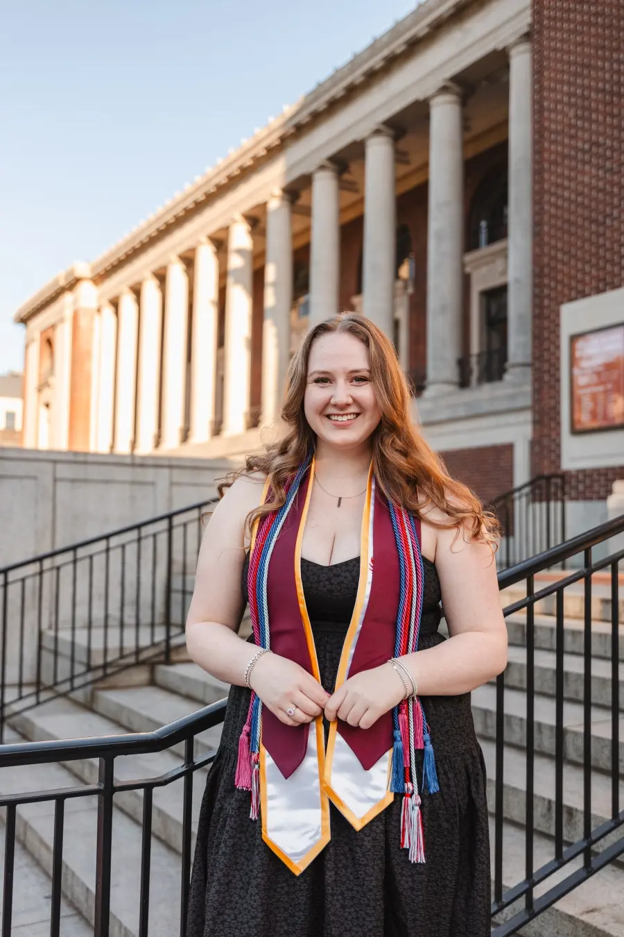 Grace smiles and poses in an HC graduation stole and cords in front of the MU.