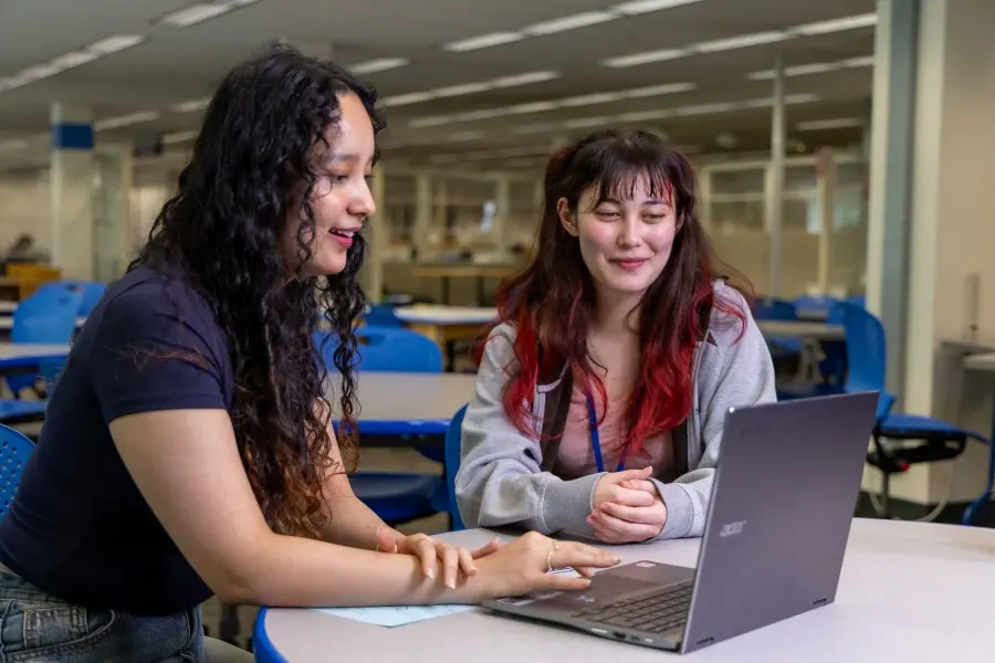 Student helping another student with work on a computer.