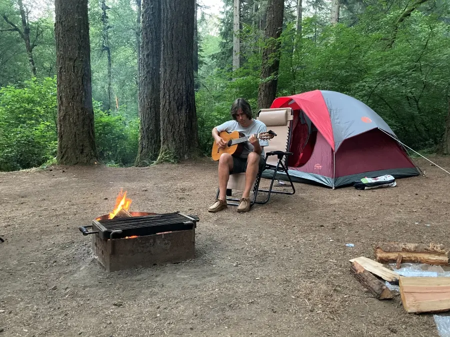Beau Baca playing a guitar at his camp site.