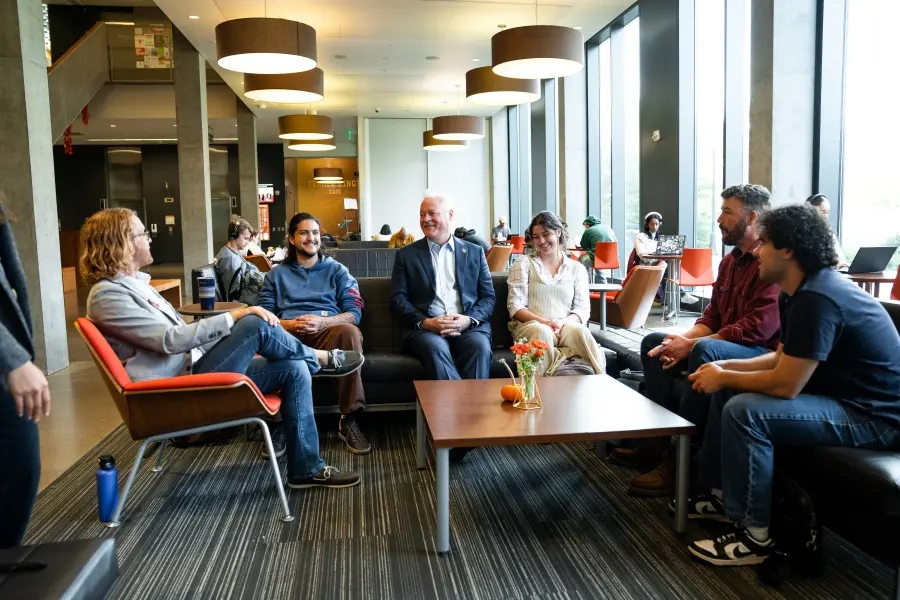 Dean of the COB Tim Caroll and students, alumni, and instructors involved in the OSU College of Business Discourse Program sit around a table in Austin Hall.