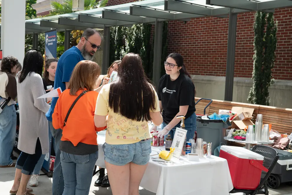 Honors student Giada Giacomini engages community members at the Honors College table during the Dam Proud Day Street Fair, where honors students sold dirty sodas.