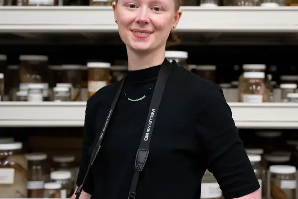 Natalie smiling in a lab with a camera around her neck