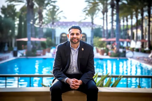 Ravi posing in a suit with a pool behind him.