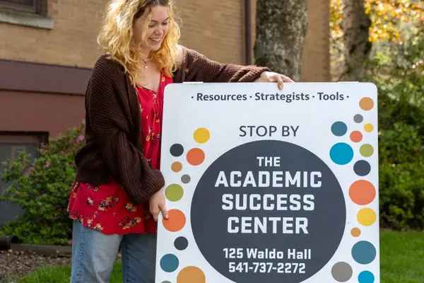 Student placing an Academic Success Center sign on the ground.