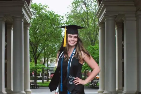 Maja Engler in her graduation cap, cords, and stole in front of Weatherford Hall