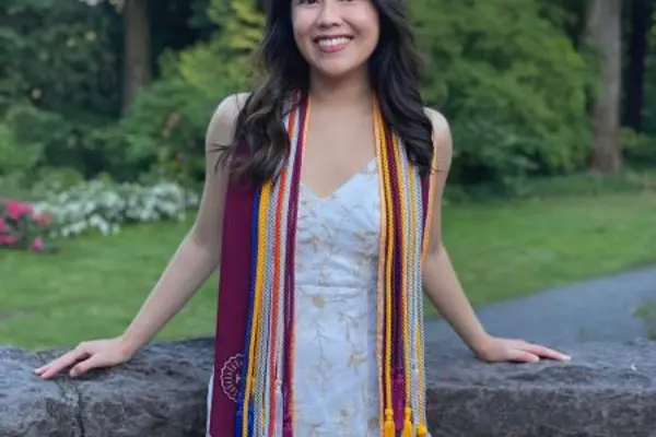 Tiffany in her graduation cords and stole with trees behind her