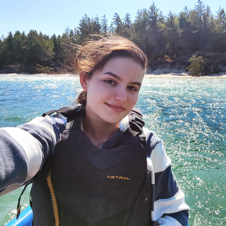 Elitca smiles, sitting on a kayak on a river.