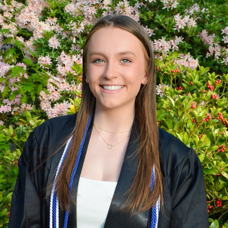 Jamie smiles for a headshot in a grad gown and cords.