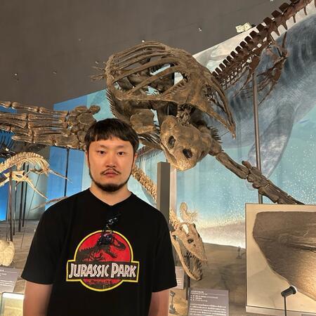 Rio stands in front of a giant tortoise fossil museum exhibit, wearing a Jurassic Park shirt.